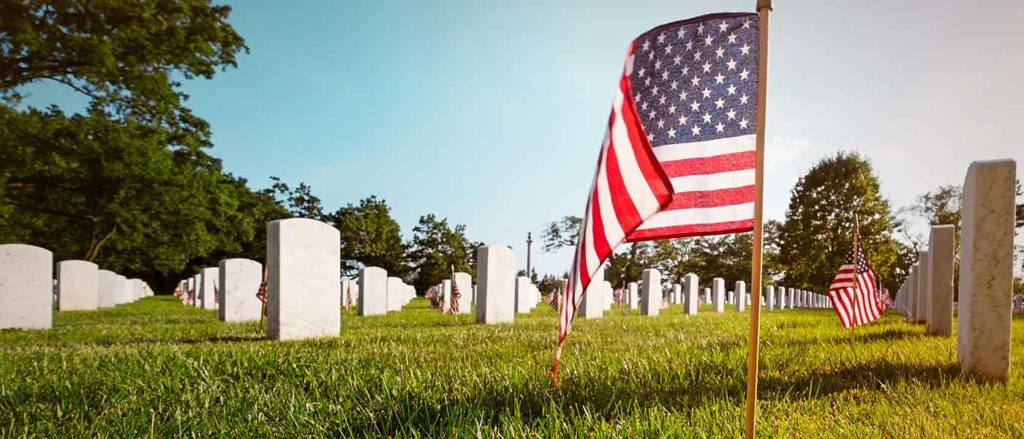 An American flag waves next to upright headstones